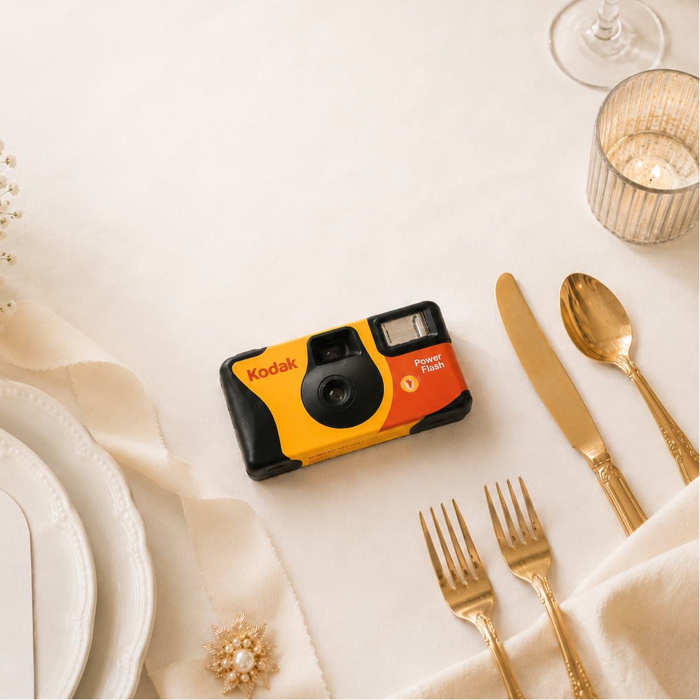 Kodak instant camera on a table setting with flowers, cutlery, and a glass.