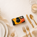 Kodak instant camera on a table setting with flowers, cutlery, and a glass.